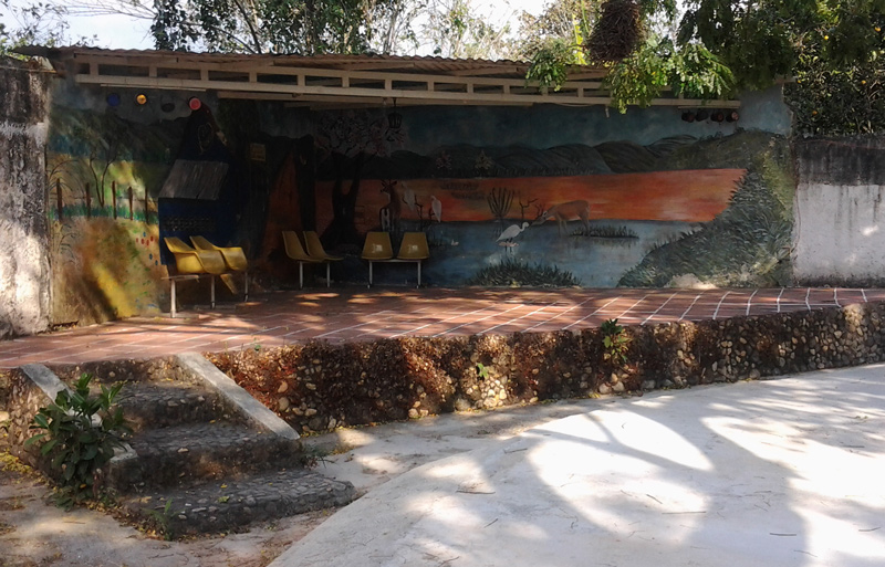 Tarima campestre al aire libre, rodeada de árboles y decorada con un original mural. El Rincón de Simón expomercio